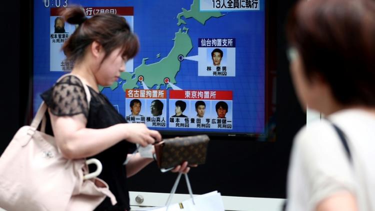 Des piétons passent devant un écran de télévision diffusant des informations sur l'exécution de six membres de la secte Aum Vérité Suprême, le 26 juillet 2018 à Tokyo [Behrouz MEHRI / AFP]