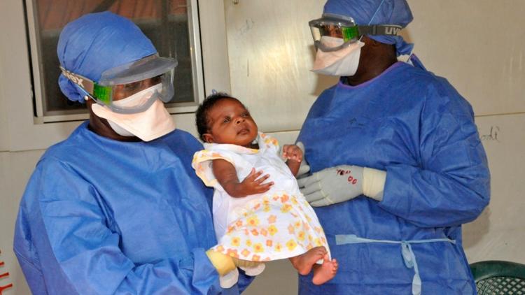 La petite Noubia dans les bras d'une soignante le 28 novembre 2015 à Conakry quelques jours après avoir été déclarée guérie du virus Ebola [CELLOU BINANI / AFP]