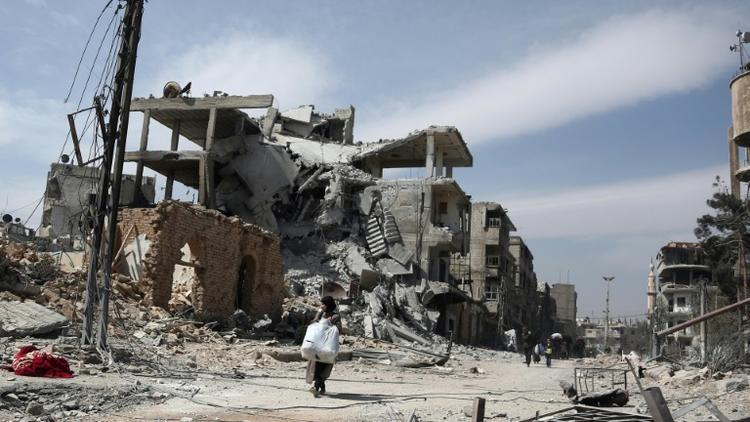 Des Syriens fuyant la localité de Hammouriyé et ses bâtiments détruits par les bombardements face à l'avancée des forces du régime, le 15 mars 2018 [ABDULMONAM EASSA / AFP]
