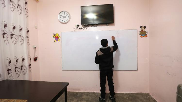 Un adolescent écrit sur un tableau au centre "Hori" pour anciens enfants jihadistes géré par les forces kurdes à Tal Maarouf, dans le nord-est de la Syrie, le 11 février 2018 [Delil souleiman / AFP]