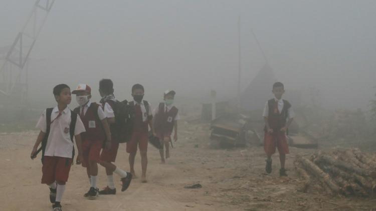Des enfants indonésiens marchent vers leur école dans l'air pollué par de gigantesques incendies de forêt à Palembang, dans l'île de Sumatra, le 14 octobre 2019 [Abdul Qodir / AFP]