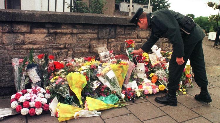 Un officier de la Royal Ulster Constabulary dépose des fleurs devant le site d'un attentat à Omagh le 17 août 1998 [Paul Vicente / AFP/Archives]
