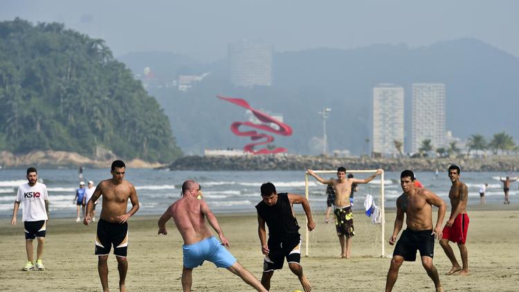 Des personnes jouent au football le 8 juin 2014, sur la plage de Santos, au Brésil, quelques jours avant le début de la Coupe du Monde de foot. [Ronaldo Schemodt / AFP]