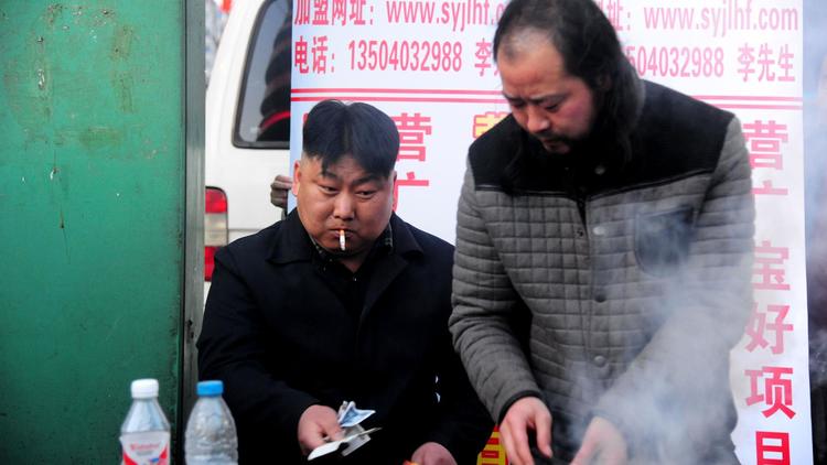 Un vendeur de brochettes (g) dont la ressemblance avec le dirigeant nord-coréen Kim Jong-Un est étonnante, attend le chaland le 22 mars 2014 derrière son barbecue dans la ville de Shenyang, au nord-est de la Chine [ / AFP]