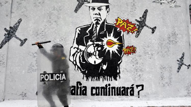 Un policier à côté d'un graffiti représentant le président colombien Juan Manuel Santos le 1er mai 2014 à Bogota [Guillermo Legaria / AFP/Archives]