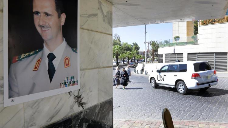 Un portrait du président syrien Bachar al-Assad sur un mur alors qu'un véhicule des inspecteurs de l'OIAC quitte un hôtel à Damas, le 9 octobre 2013 [Louai Beshara / AFP]