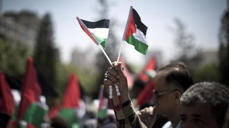 Un Palestinien brandit des drapeaux nationaux lors d'une manifestation en faveur d'une autre tentative de réconciliation entre les rivaux, le mouvement islamiste Hamas et l'organisation de libération de la Palestine (OLP) le 22 avril 2014 à Gaza [Mahmud Hams / AFP]