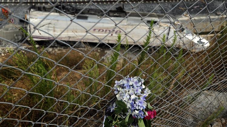 Des fleurs en hommage aux victimes de la catastrophe ferroviaire de Saint-Jacques de Compostelle avec en arrière-plan la locomotive, le 27 juillet 2013 [Rafa Rivas / AFP]