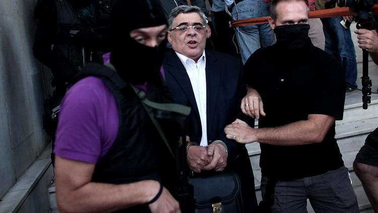 Nikos Michaloliakos entouré de policiers masqués à la sortie des locaux de la police le 28 septembre 2013 à Athènes [Angelos Tzortzinis  / AFP]