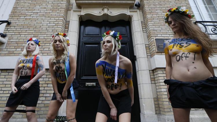 Des militantes du groupe féministe Femen urinent le 1er décembre 2013 sur une photo du président Viktor Ianoukovitch, devant l'ambassade d'Ukraine à Paris [Thomas Samson / AFP]