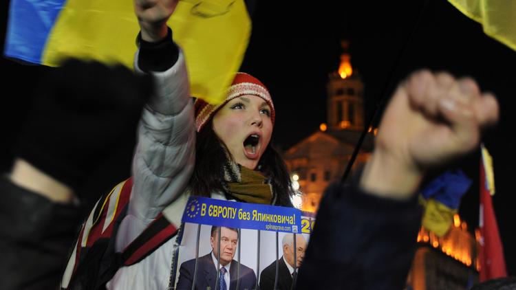 Une manifestante tient une affiche montrant le président ukrainien Viktor Ianoukovitch et le Premier ministre Mykola Azarov derrière des barreaux de prison, le 4 décembre 2013 place de l'Indépendance à Kiev [Viktor Drachev / AFP]
