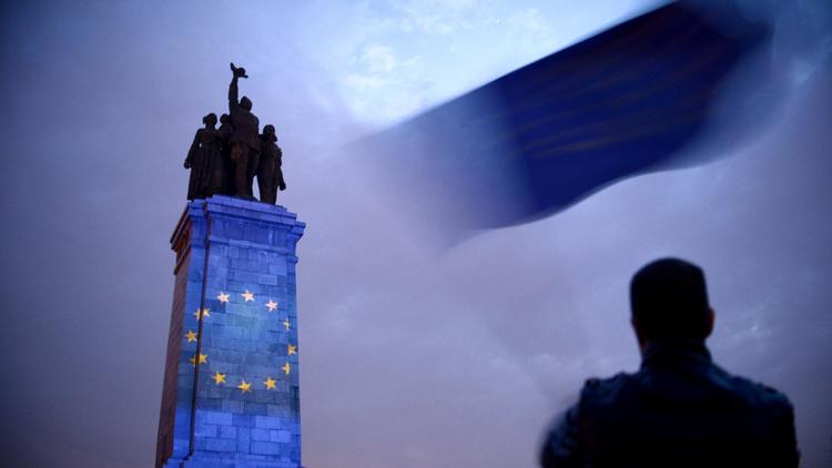 Symbole du tiraillement de la Bulgarie, à Sofia, le 8 mai 2014, un homme agite un drapeau européen devant le monument dédié à l'armée soviétique, illuminé par les étoiles jaunes sur fond bleu, symbolisant.. l'Europe [Nikolay Doychinov / AFP]