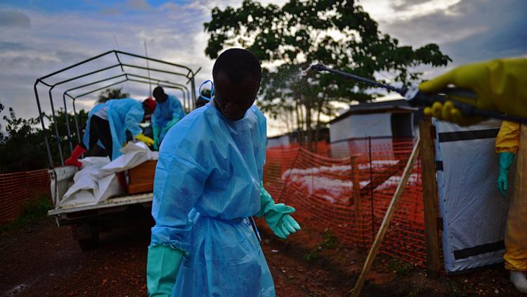 Un membre des services publics de fossoyeurs en Sierra Leone est aspergé de désinfectant tandis que des collègues chargent un camion des corps de victimes du virus Ebola, à Kailahun, le 14 août 2014 [Carl de Souza / AFP]