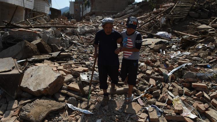 Une personne âgée, réchapée du séisme,  aidée par son petit fils dans les décombres à Longtoushan dans la province du Yunnan au sud-est de la Chine, le 7 août 2014  [Greg Baker / AFP]