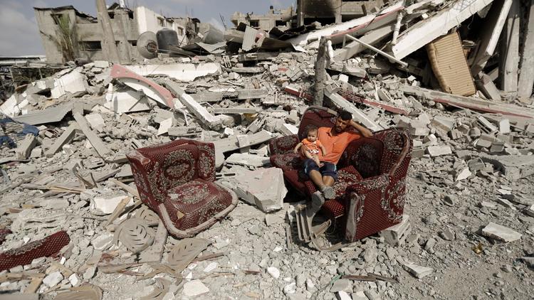 Un Palestinien assis sur un sofa avec un enfant au milieu d'un champs de ruines à Al-Shejaea (banlieue de Gaza City), le 5 août 2014 [Mohammed  Abed / AFP]