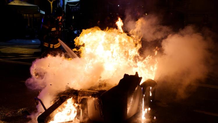 Un pompier éteint l'incendie d'une poubelle après des affrontements entre des manifestants et la police le 25 mars 2018 à Barcelone [LLUIS GENE                           / AFP]