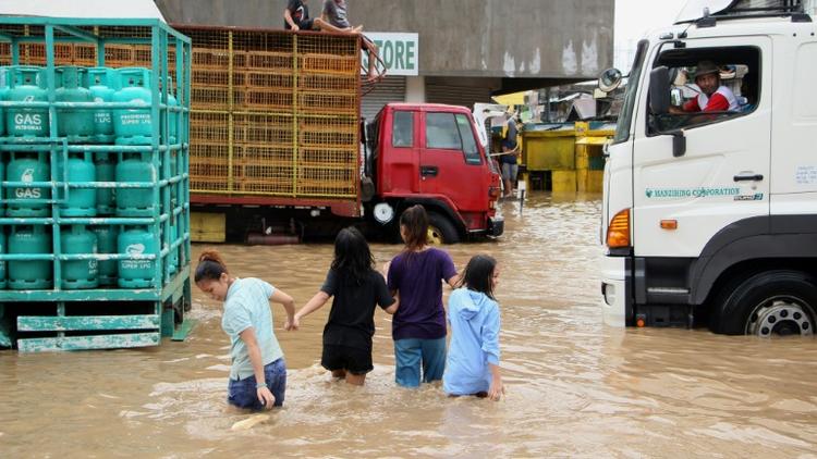 Des habitants de la ville de Baao marchent les rues inondées après le passage de la tempête Usman, le 30 décembre 2018 [Simvale SAYAT / AFP]