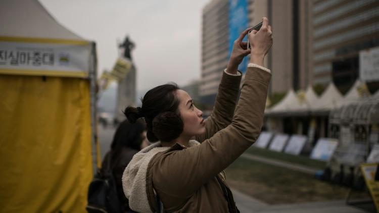 Une femme prend en photo une manifestation anti-gouvernementale, dans le centre de Séoul, le 3 novembre 2016 [Ed Jones / AFP]