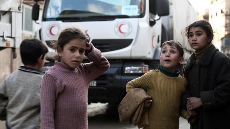 Des enfants syriens devant un convoi d'aide humanitaire du croissant rouge à Kafr Batna, dans les environs de Damas, le 23 février 2016 [AMER ALMOHIBANY / AFP/Archives]