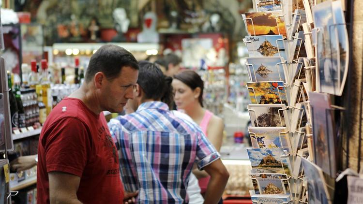 Un touriste regarde des cartes postales dans une rue du Mont-Saint-Michel [Charly Triballeau / AFP/Archives]