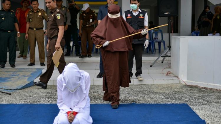 Une éxécutrice sur le point de flageller en public une femme agenouillée, le 10 décembre 2019 à Aceh, en Indonésie [CHAIDEER MAHYUDDIN / AFP]