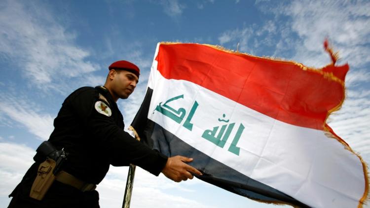 Un policier irakien devant le drapeau de l'Irak, à Najaf le 9 janvier 2016 [HAIDAR HAMDANI / AFP/Archives]