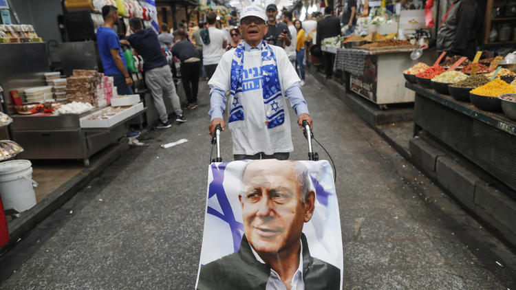Un partisan du Likoud pousse un chariot recouvert d'une affiche représentant le Premier ministre israélien Benjamin Netanyahou, le long d'une allée du principal marché de Jérusalem le 8 avril 2019, un jour avant les élections.